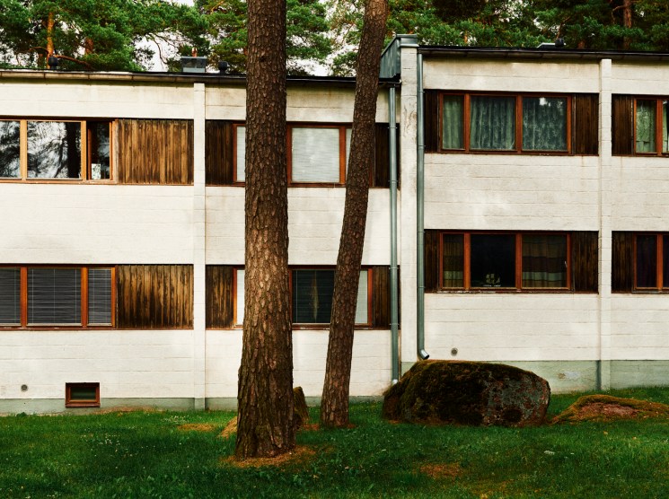 White modernist building among pine trees on a green lawn.