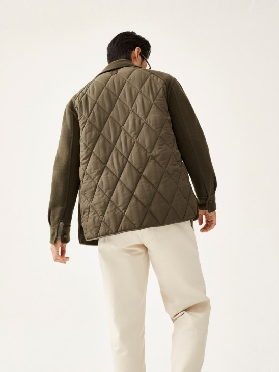 Model wearing olive quilted jacket and cream trousers, shown from behind against white background