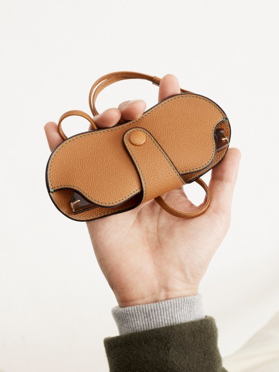 Hand holding a small tan leather elephant-shaped glasses case with handles against a light background