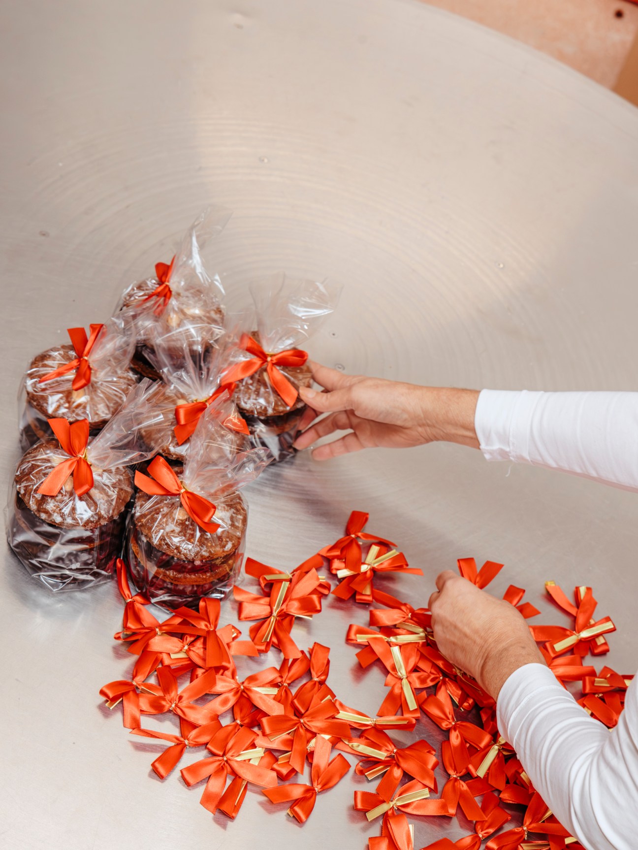 Hands packaging traditional German Lebkuchen gingerbread cookies in clear bags tied with bright orange ribbons
