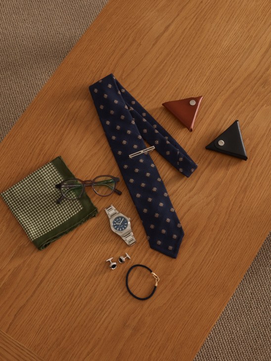 Collection of men's accessories including tie, glasses, watch, cufflinks and bracelet arranged elegantly