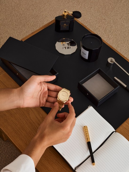 Luxury desk setup with automatic watch, leather accessories, grooming products, candles, and writing instruments