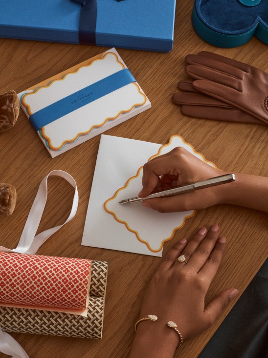 Elegant writing accessories including fountain pen, stationery, jewelry, and gift wrapping materials arranged on a surface