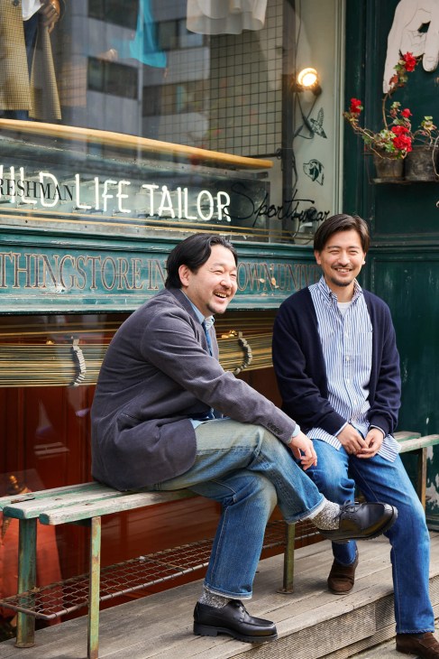 Two men sitting outside Wild Life Tailor shop storefront, one wearing blazer, one in cardigan