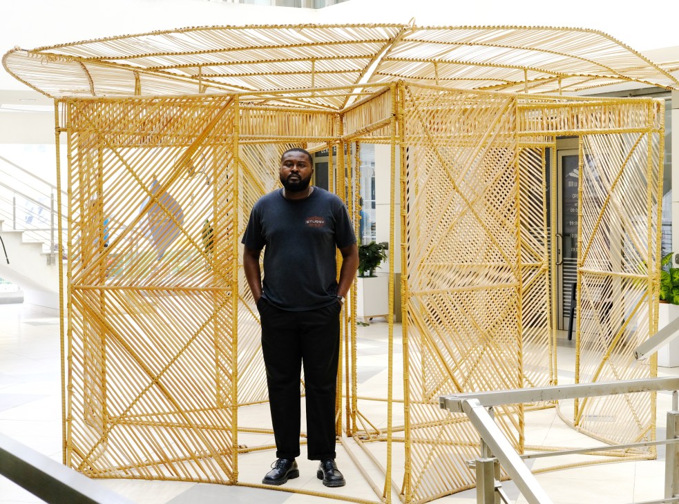 Nifemi Marcus-Bello standing beside geometric golden bamboo structure in gallery space