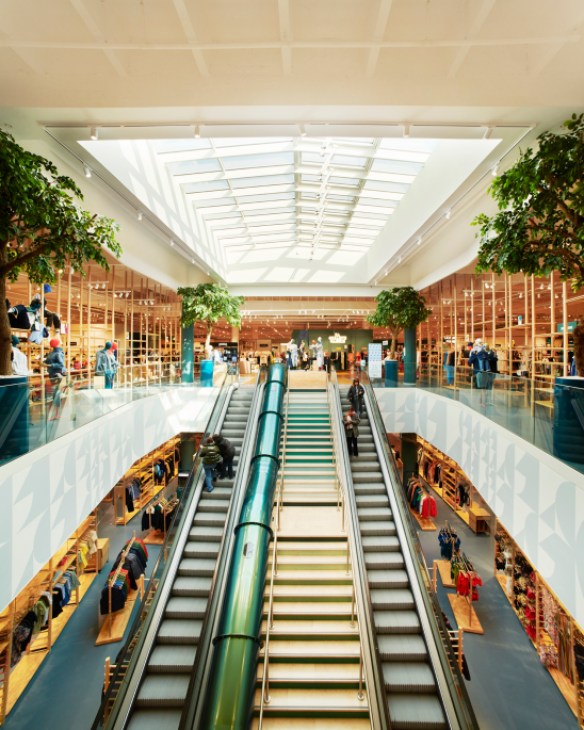 Modern shopping center interior with escalators, skylight, and multi-level retail spaces with wooden fixtures