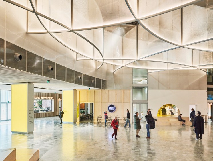 Modern interior with curved metal sculptural installation overhead and people walking through bright open space