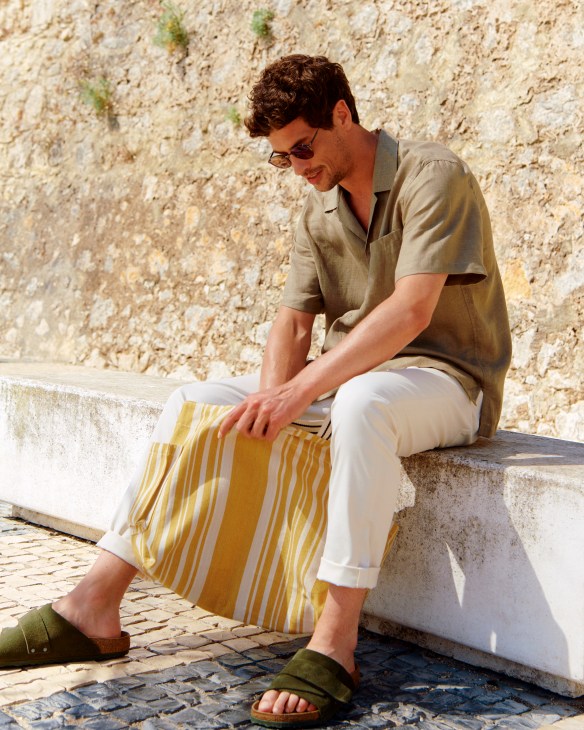 Man in white shirt and jeans with sandals and sunglasses carrying tote bag