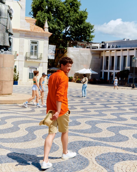 Man in blue shirt and beige shorts with white sneakers and hat