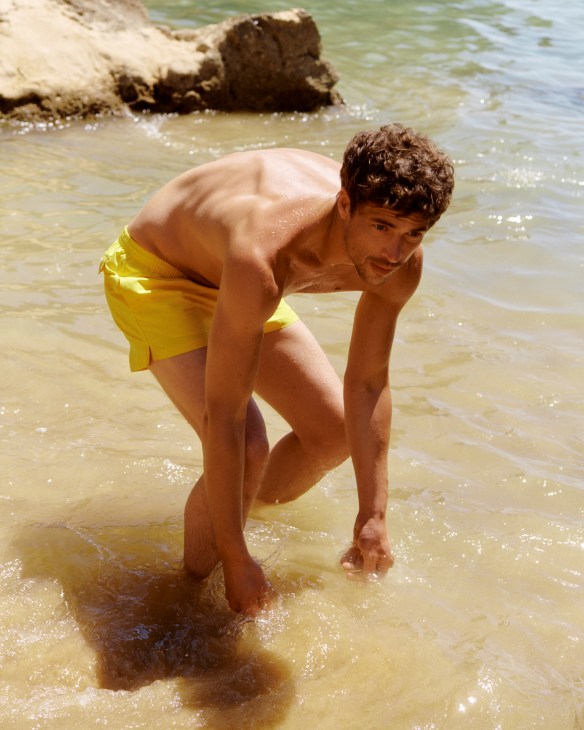 Man in yellow and blue patterned swim shorts against yellow wall