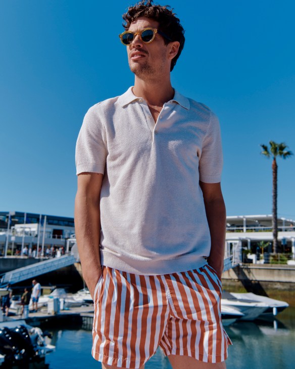 Man in white polo shirt and orange swim shorts with sunglasses