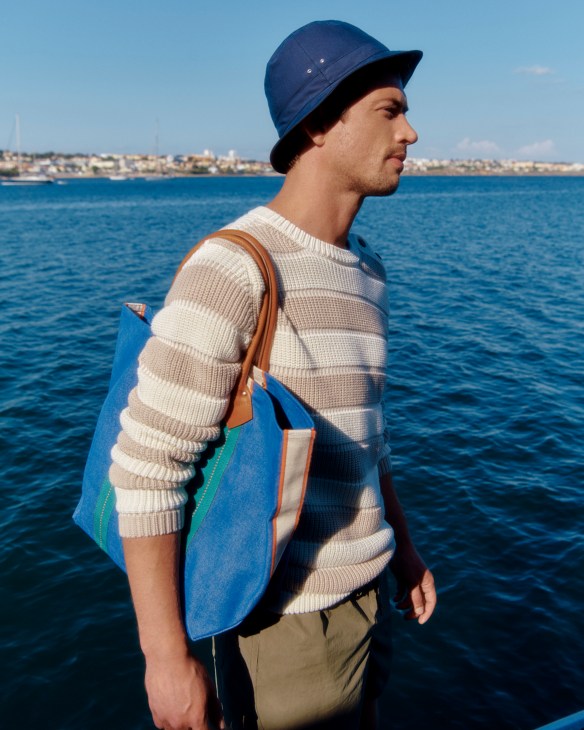 Man in white sweater and patterned shorts with hat and bag