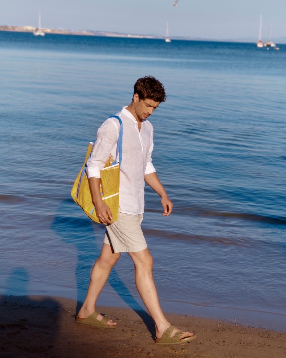 Man in white shirt and beige shorts carrying shoulder bag