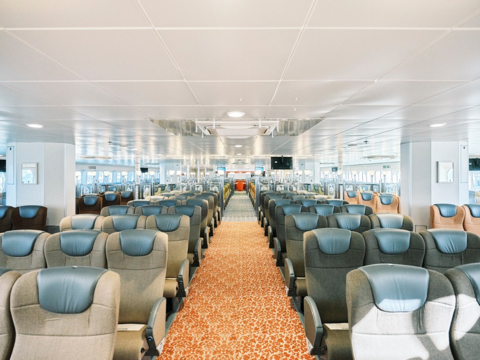 Interior view of Queen Beetle ferry's standard class passenger seating area with blue and gray chairs