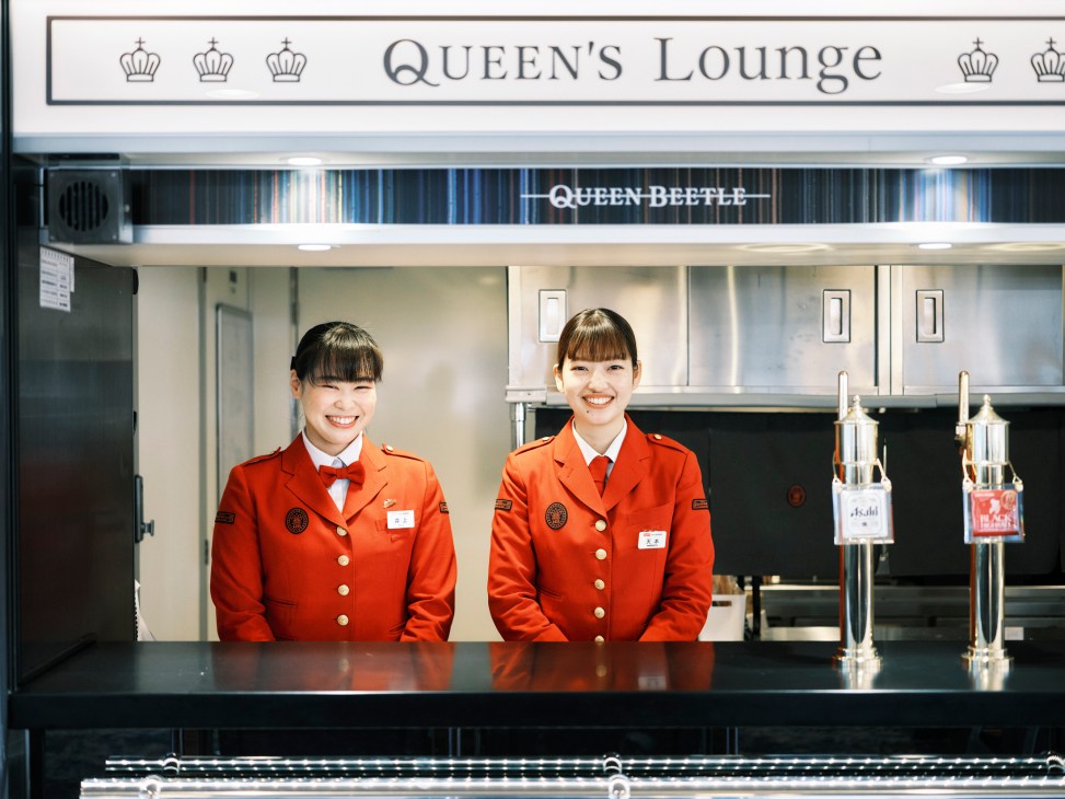 Two smiling ferry staff members in red uniforms standing behind a bar counter with beer taps