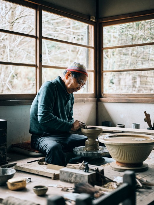 Potter Genta Yamamoto working at his pottery wheel in his workshop near large windows
