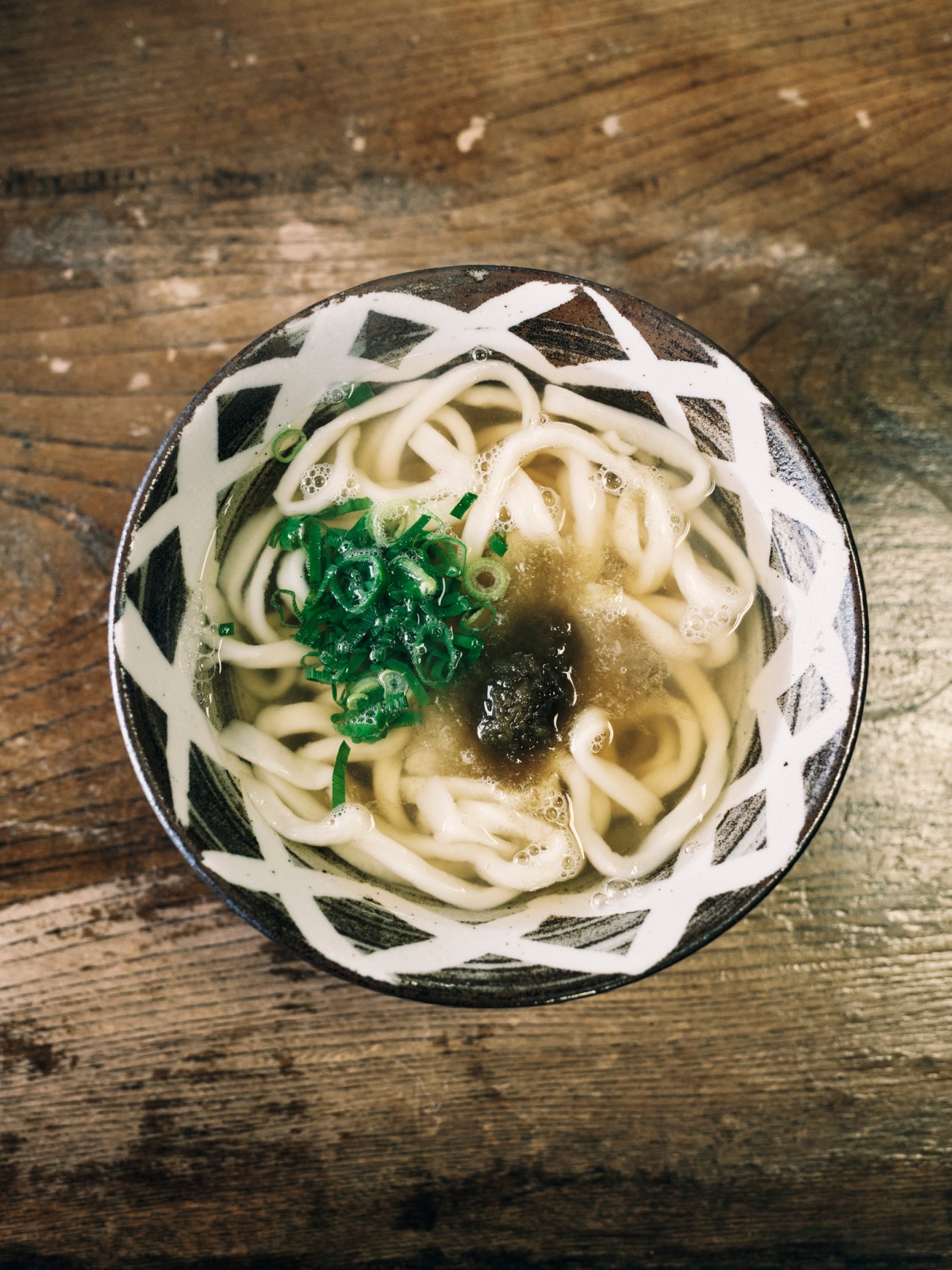 Bowl of udon noodles in clear broth with green seaweed garnish served in decorative ceramic bowl