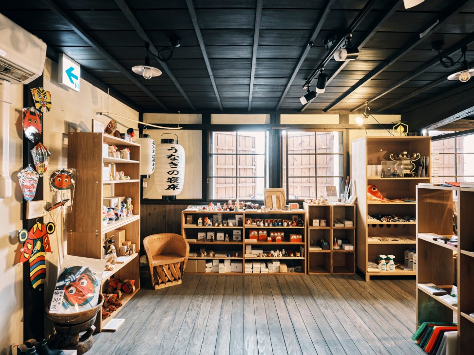 Interior of a Japanese craft shop with wooden shelves displaying ceramics, traditional items, and colorful masks on walls