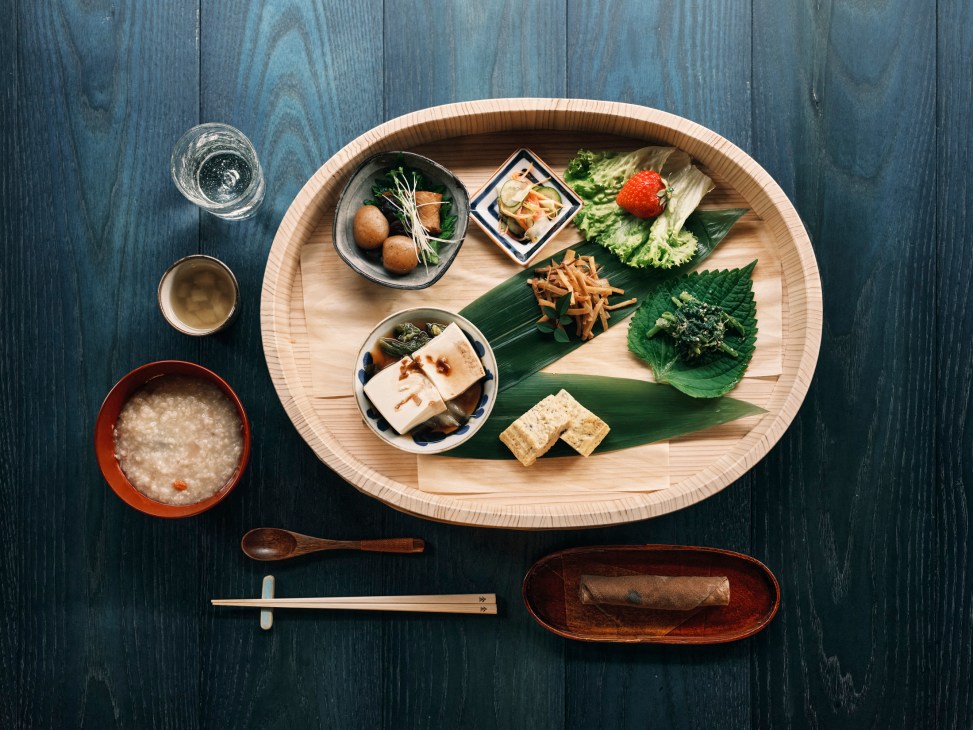Traditional Japanese meal beautifully arranged on wooden tray with various small dishes, tofu, vegetables and accompaniments