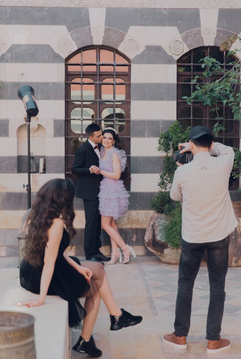 A couple posing for a photographer in formal attire against historic stone architecture