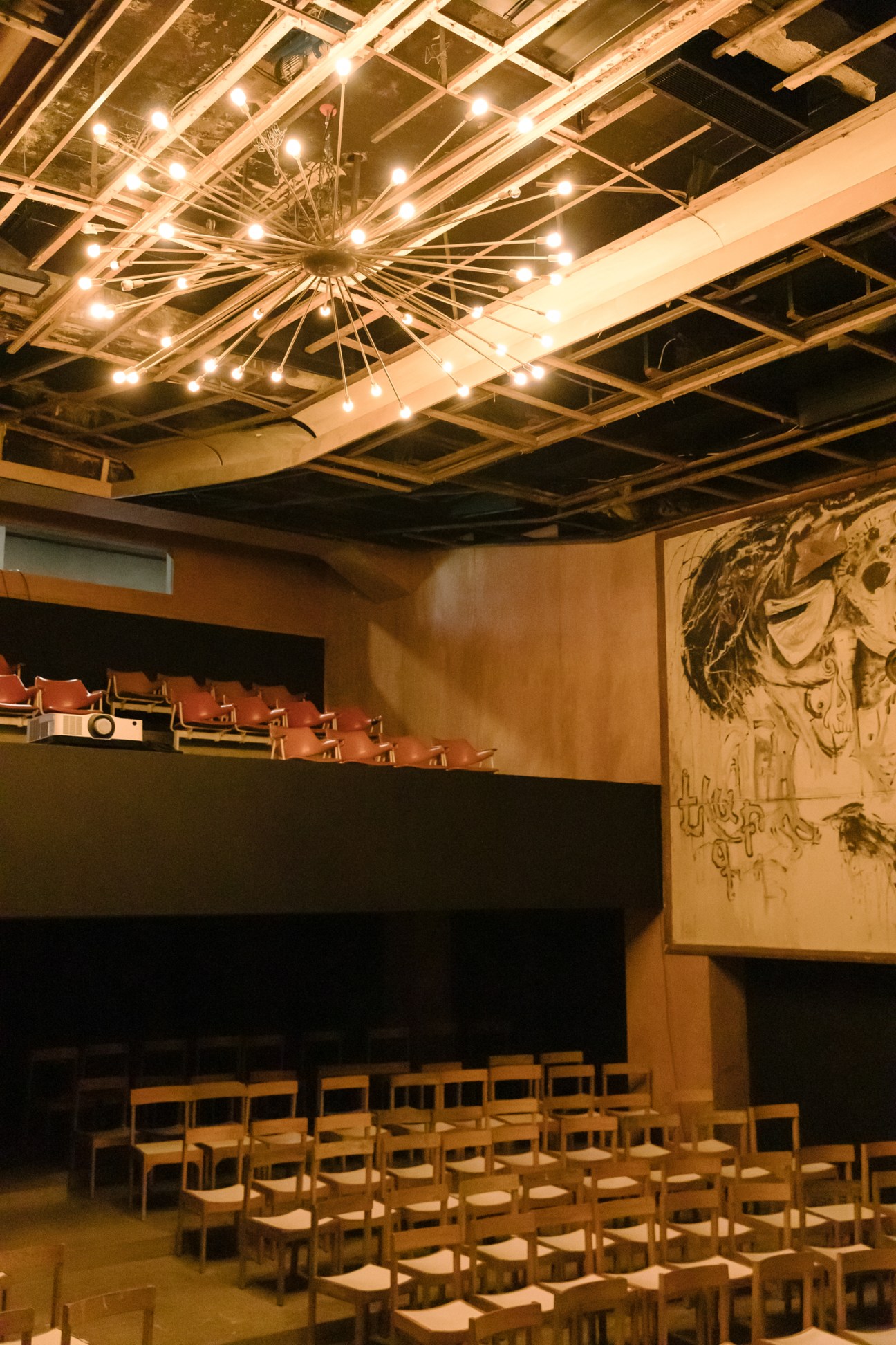 Interior of Cinema Royal screening room with exposed ceiling beams, string lights, tiered seating and wall mural