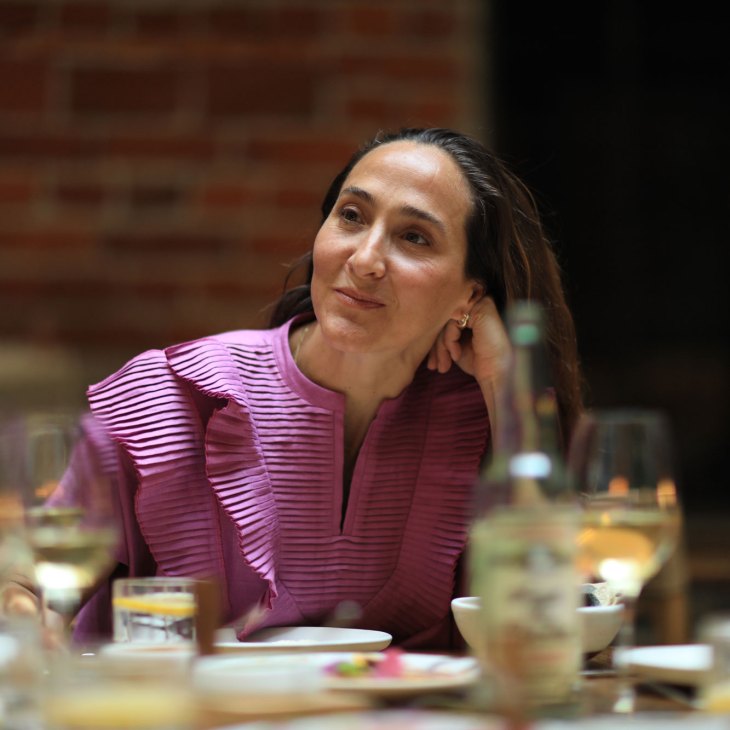 Woman in purple pleated top smiling while seated at restaurant table with drinks and plates