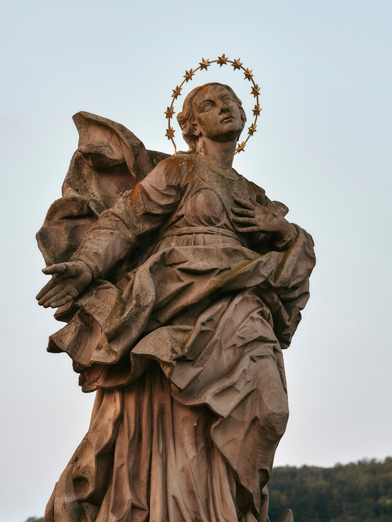 Stone statue of winged figure with halo of golden stars against overcast sky
