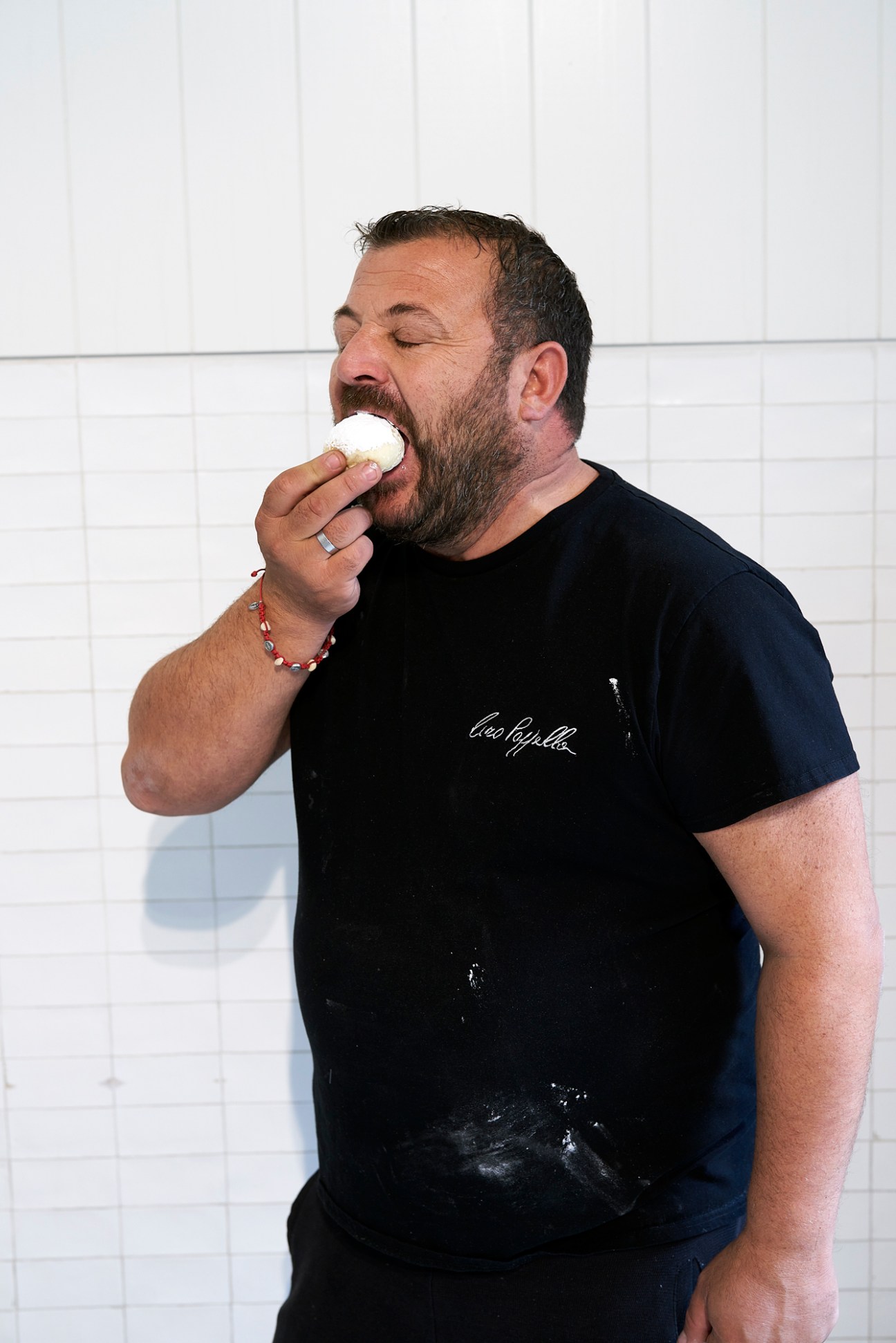 Ciro Scognamillo eating a white pastry in his bakery kitchen wearing a black t-shirt