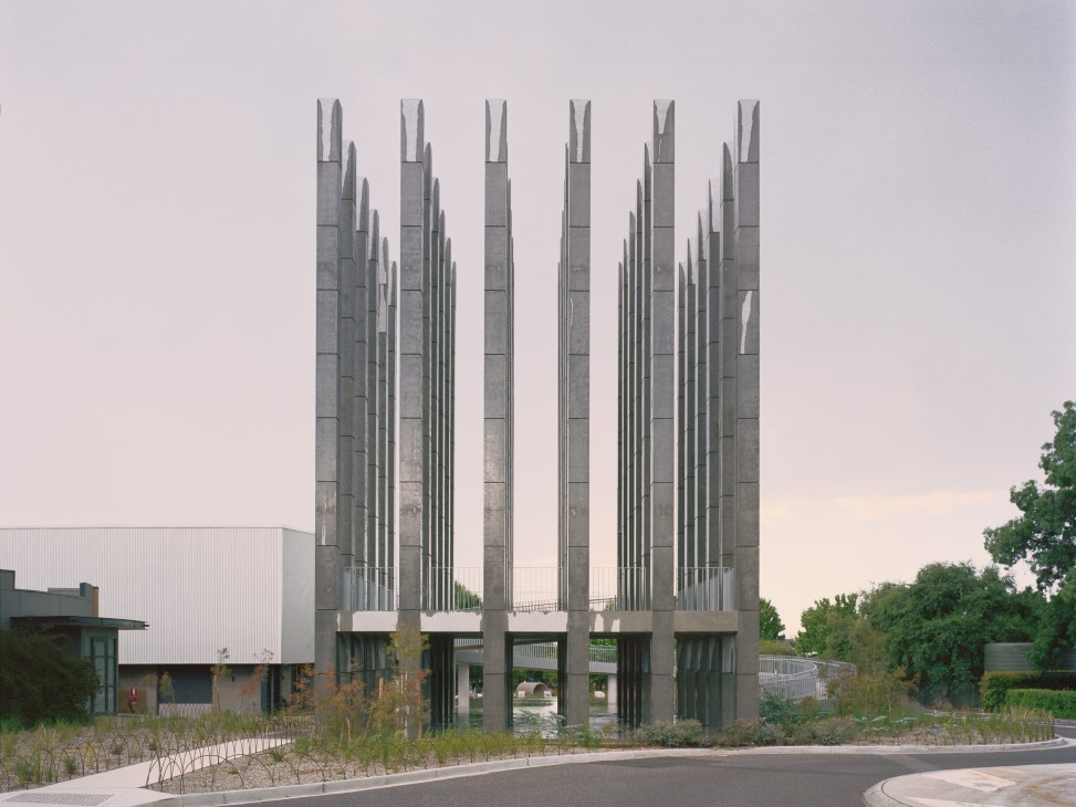 Towering concrete columns arranged in a symmetrical grid with surrounding vegetation at the "Less" installation in Canberra.