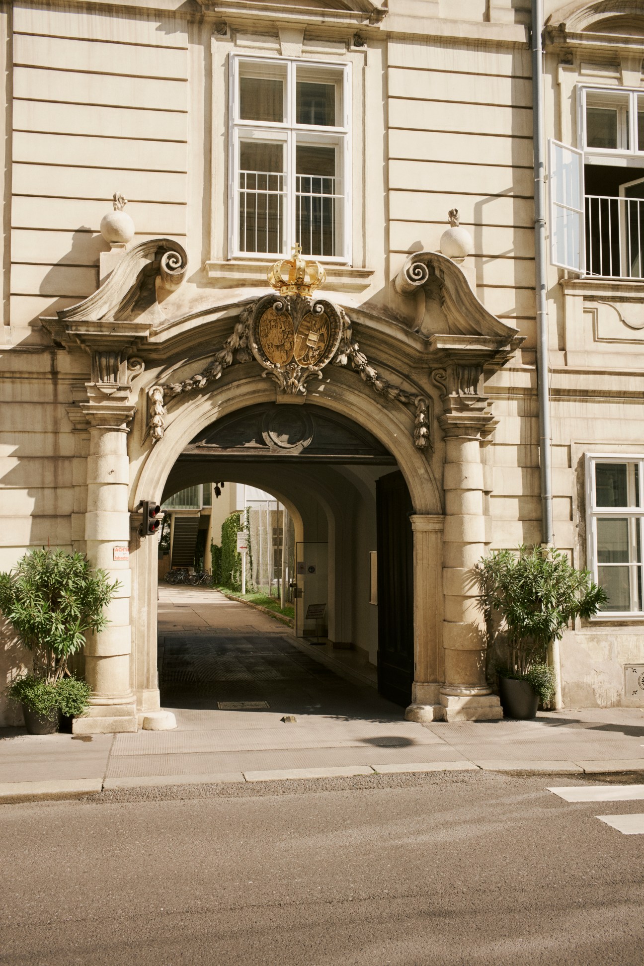 Ornate baroque entrance archway with imperial coat of arms and crown, flanked by columns and potted plants
