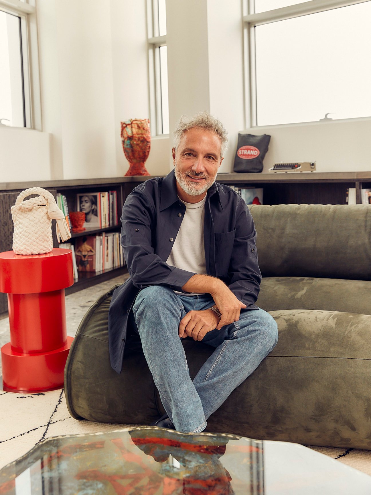 Leo Rongone, CEO of Bottega Veneta, sitting on a grey sofa in a modern office with bookshelves and decorative objects