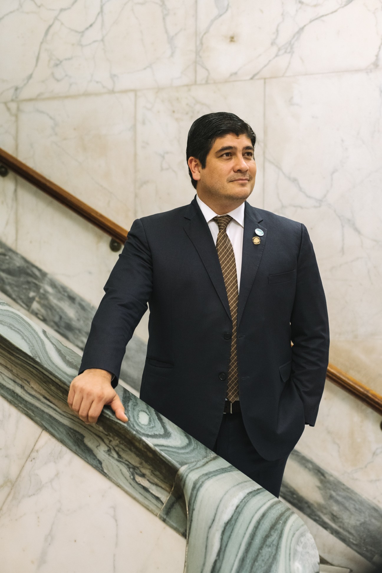 Carlos Alvarado Quesada in a dark suit standing on marble stairs in an ornate building