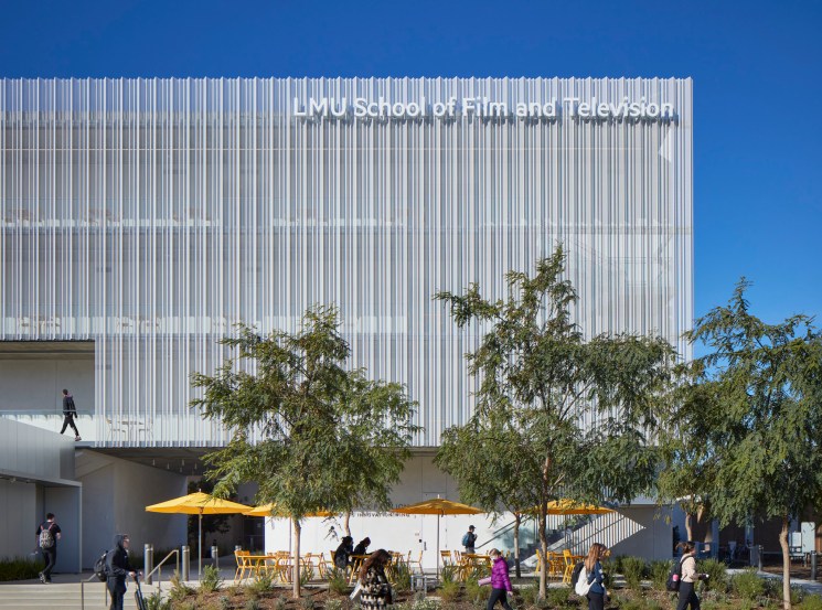 Modern university building with vertical metal cladding and students walking outside with yellow umbrellas