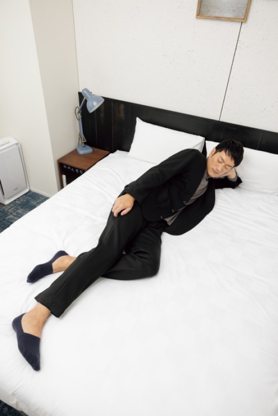 Person in dark business suit lying on hotel bed in relaxed position