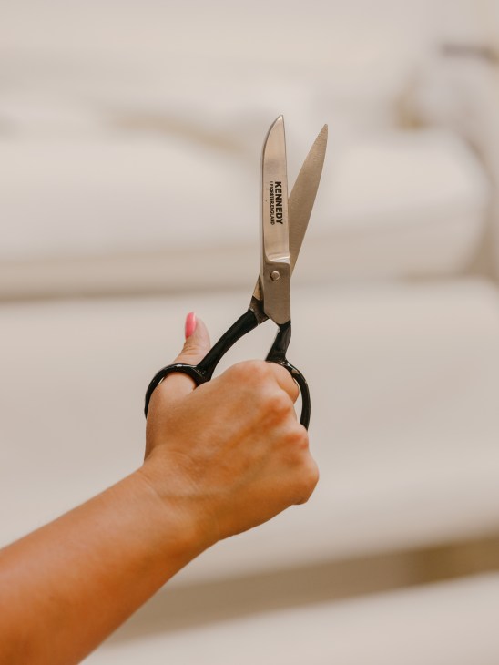Hand holding scissors cutting high-quality waxed cotton fabric with precision