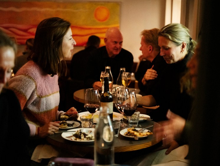 People dining at a restaurant table with wine glasses, plates of food, and warm lighting