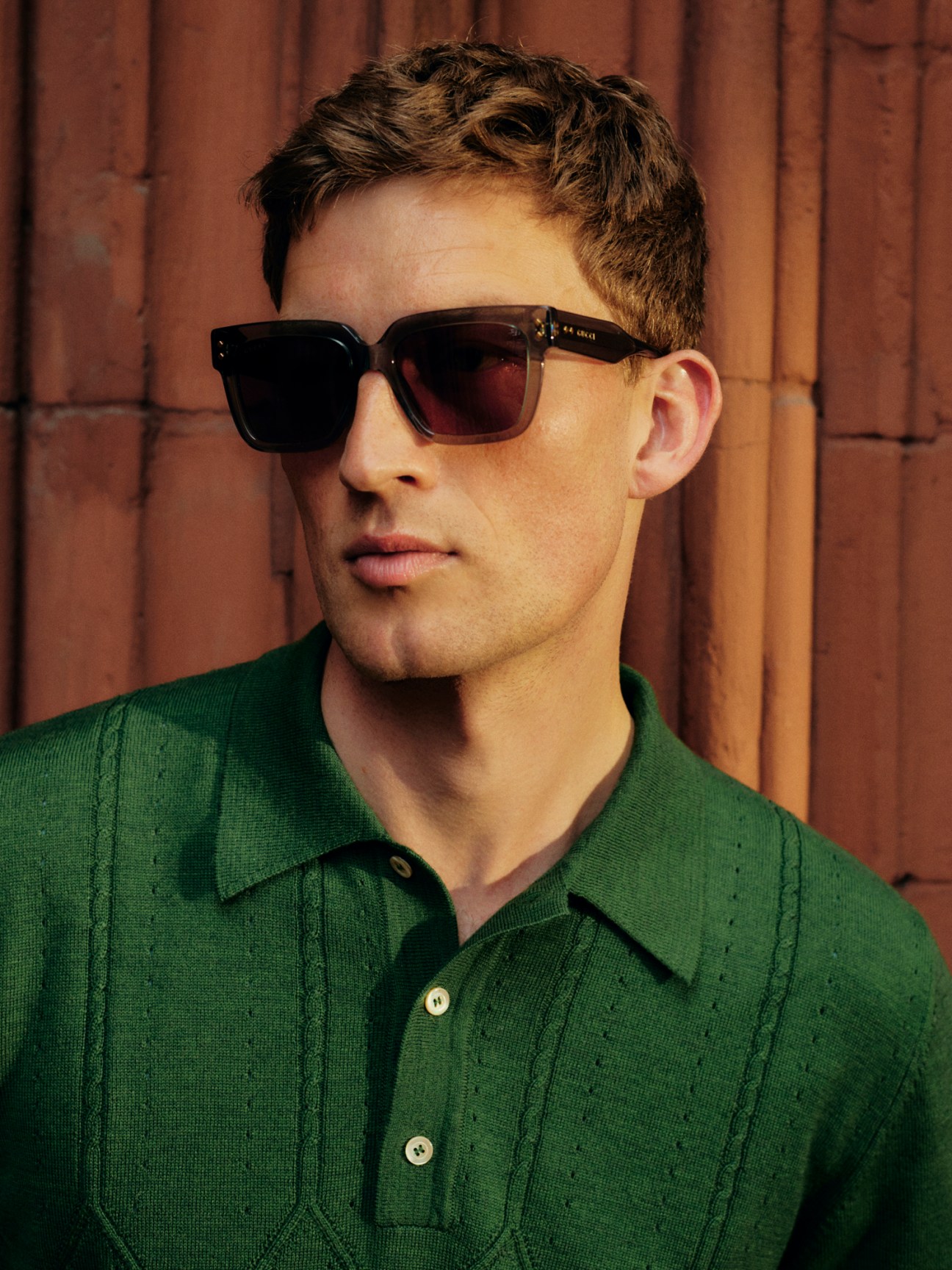 Model wearing green polo shirt and dark sunglasses against wooden background
