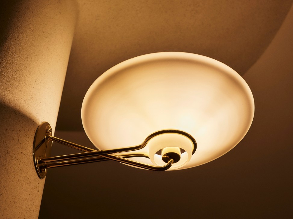 Elegant brass wall sconce with circular shade mounted on warm-toned wall in entrance hall