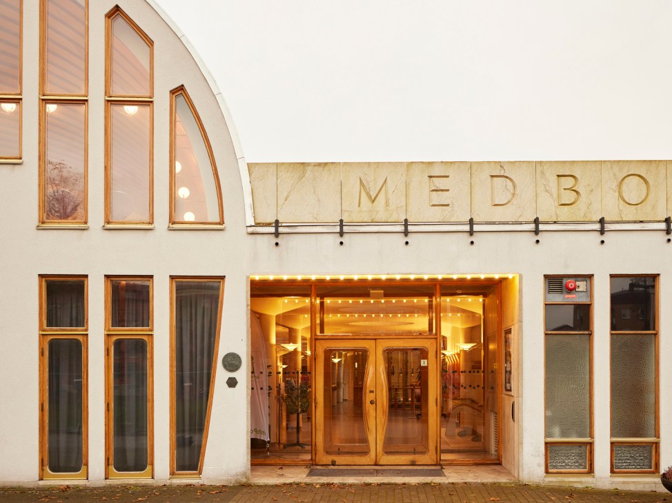 White modernist building exterior with wooden-framed windows and illuminated entrance displaying 'MEDBOR' lettering