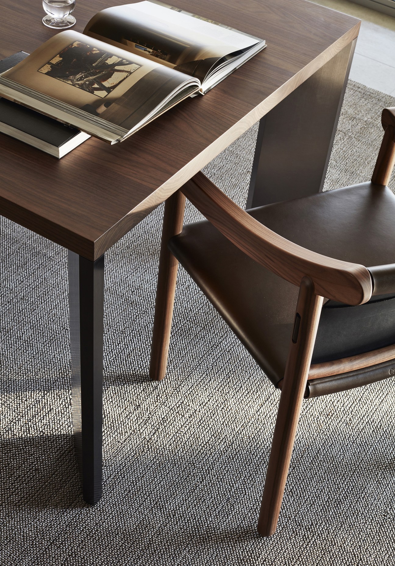 Cassina 905 chair by Vico Magistretti with wood frame and black leather seat at dark wood desk with open magazine.