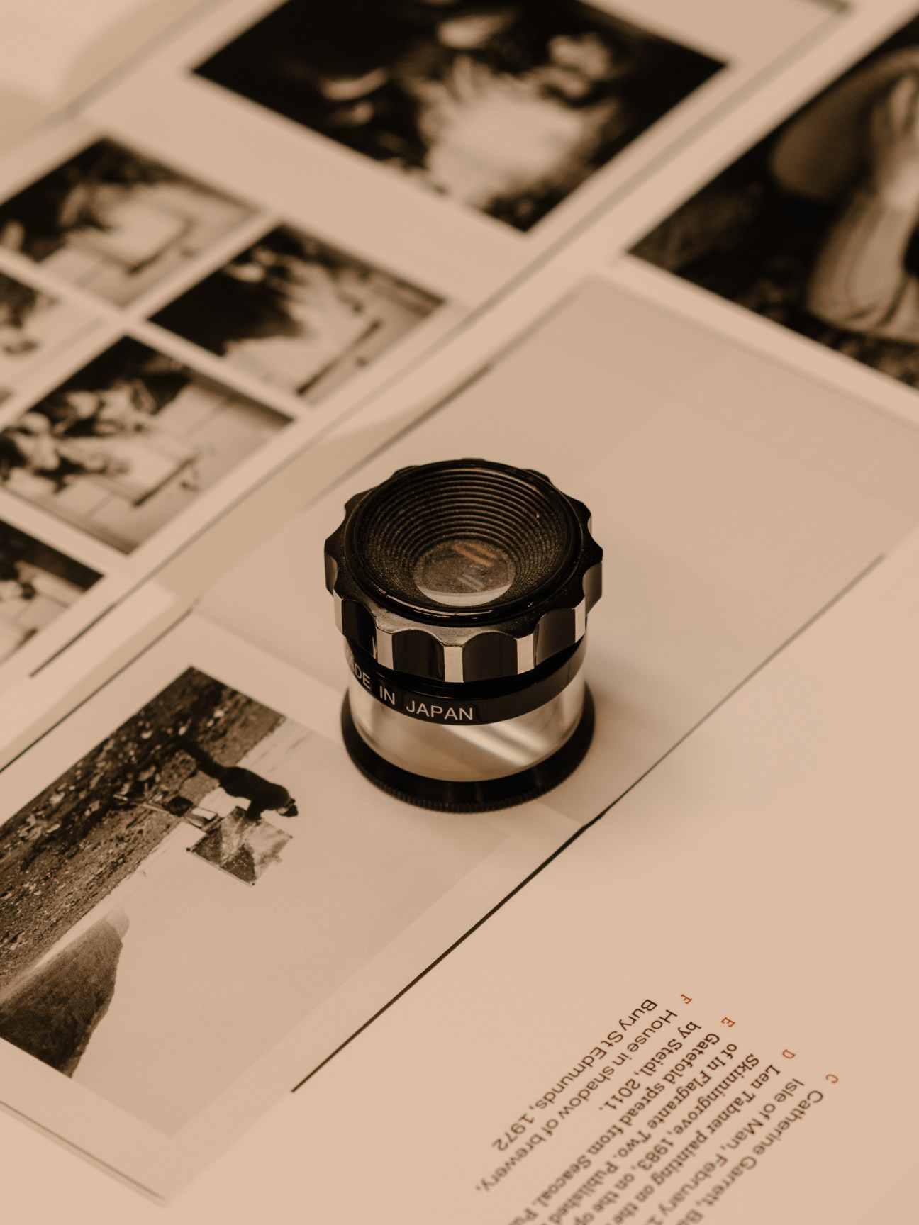 A precision loupe magnifying glass sits on vintage black and white photographs, with 'Made in Japan' visible on the device