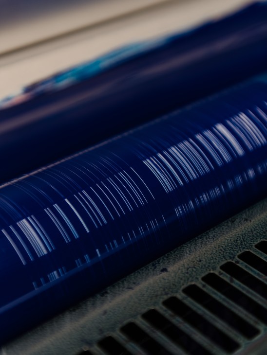 Close-up of blue ink being applied to printing plate with vertical striped pattern in printing press