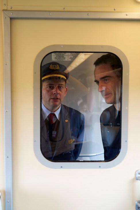 Train conductor in uniform cap speaking with passenger through window of vintage Italian railway car