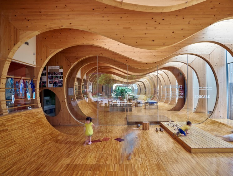 Children playing inside a flowing curved timber tunnel structure.