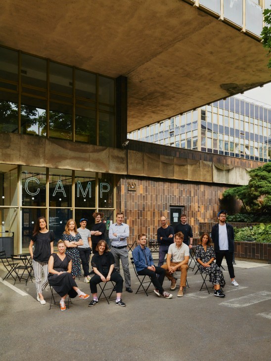 Group of designers and architects sitting and standing outside modern concrete building with CAMP signage