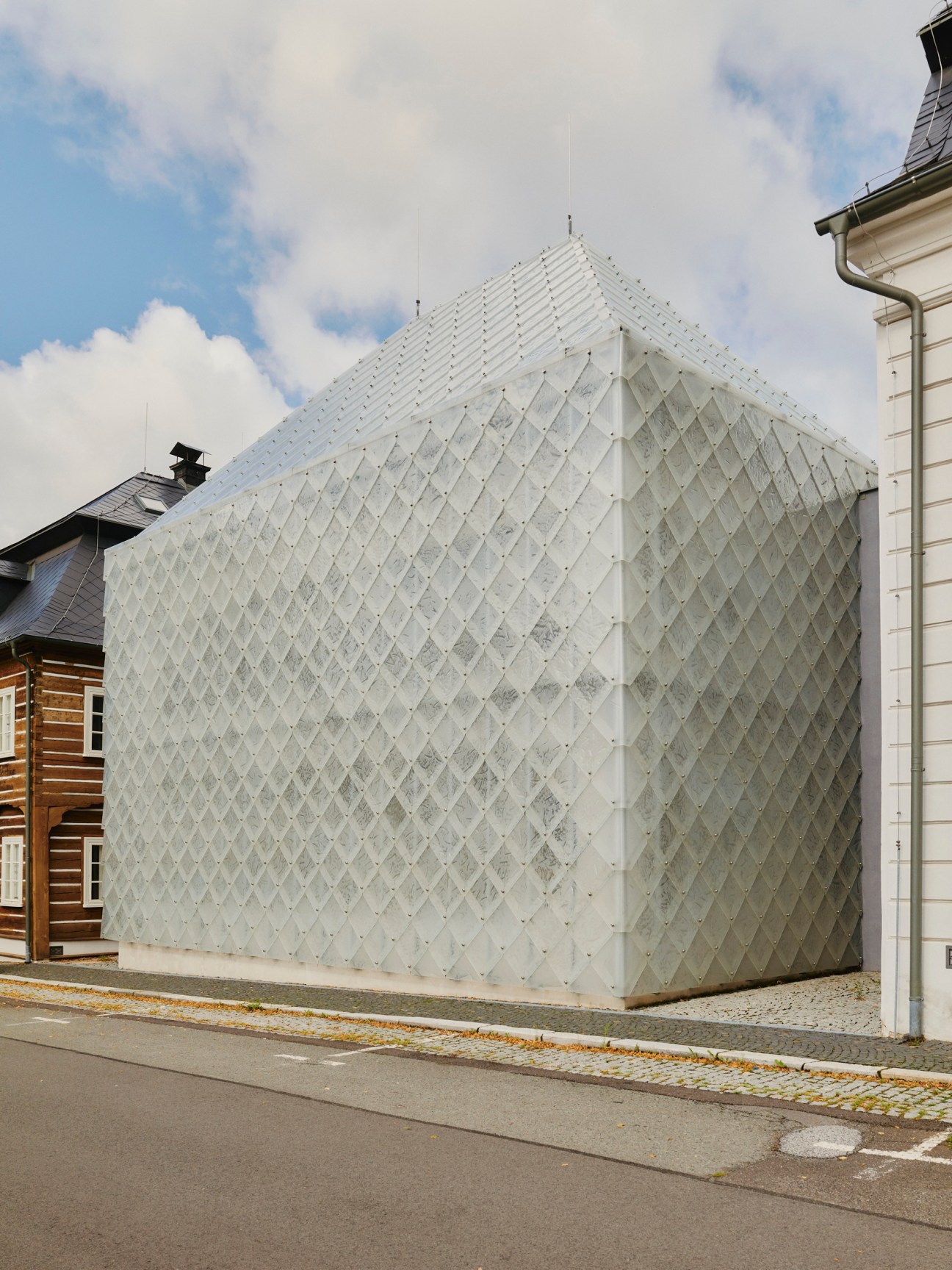 Translucent white modernist building with geometric diamond pattern facade and pitched roof in Novy Bor.