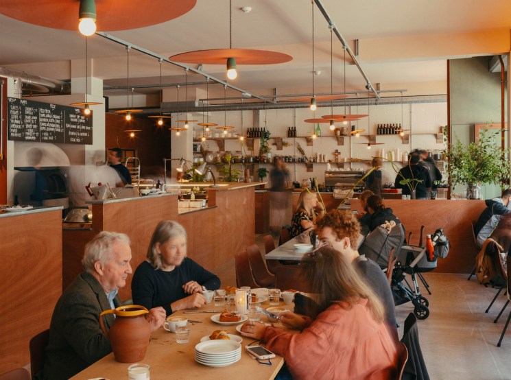 Interior of Big Jo bakery showing diners at communal tables with orange pendant lights and open kitchen