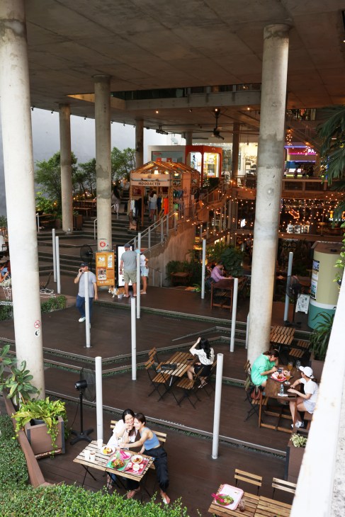 Multi-level food hall with concrete columns, wooden tables, diners eating, and string lights