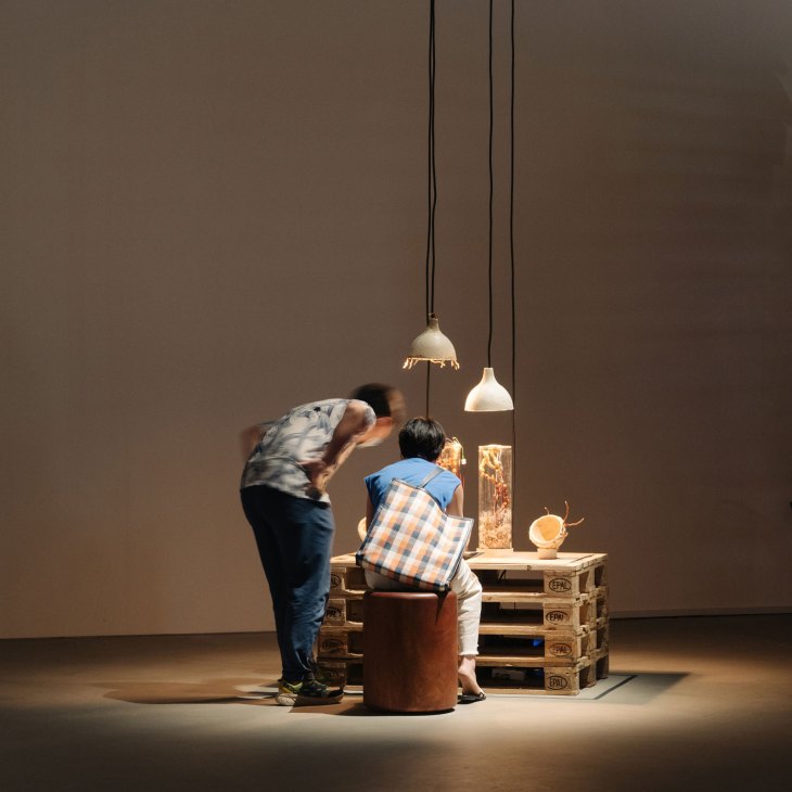 Two people examining artworks at a makeshift table made from wooden pallets under pendant lights