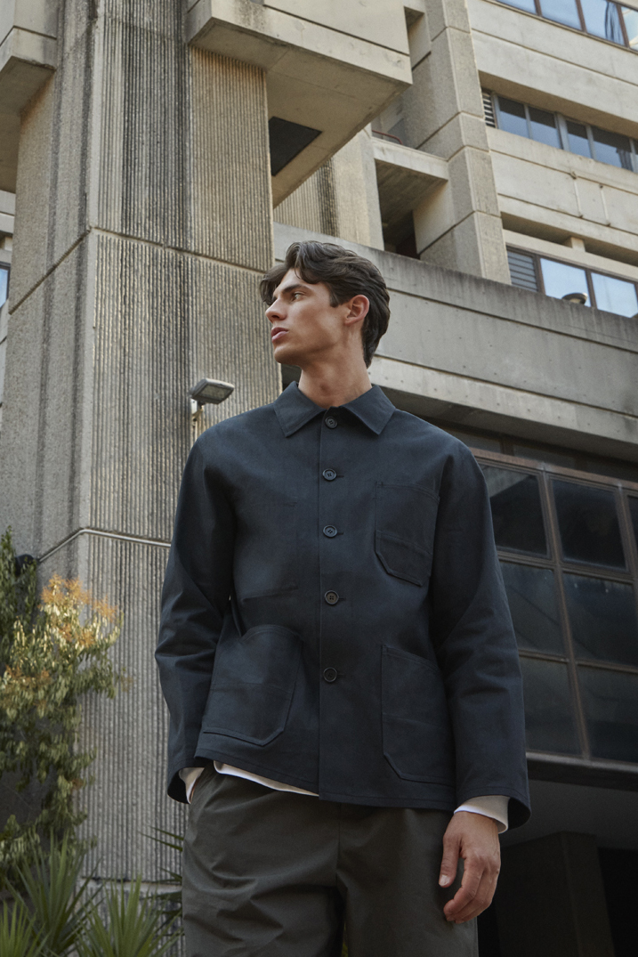 Man in dark navy button-up jacket looking upward against concrete building background